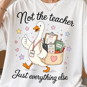 May include: A white t-shirt featuring a cartoon goose wearing a lanyard with a tag labeled PARA. The goose holds a bag containing a clipboard labeled IEP, a device labeled AAC, a notebook labeled DATA, and an apple. Text reads Not the teacher Just everything else.