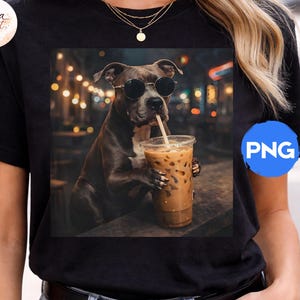 May include: Black t-shirt featuring a dog wearing sunglasses and drinking an iced coffee. The dog is the central focus, with a blurred background of lights and a bar setting. The shirt has a round neck and short sleeves.