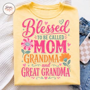 May include: Pale yellow t-shirt featuring the text "Blessed to be called Mom, Grandma, and Great Grandma" in pink and orange, with floral and heart motifs. A relaxed-fit top.