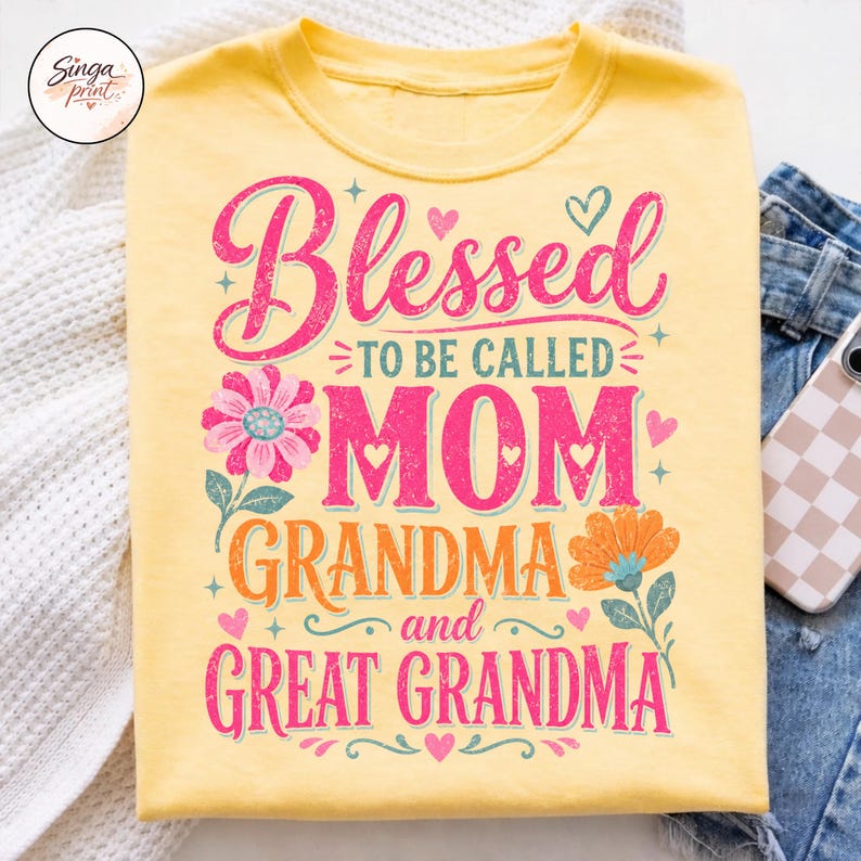 May include: Pale yellow t-shirt featuring the text "Blessed to be called Mom, Grandma, and Great Grandma" in pink and orange, with floral and heart motifs. A relaxed-fit top.