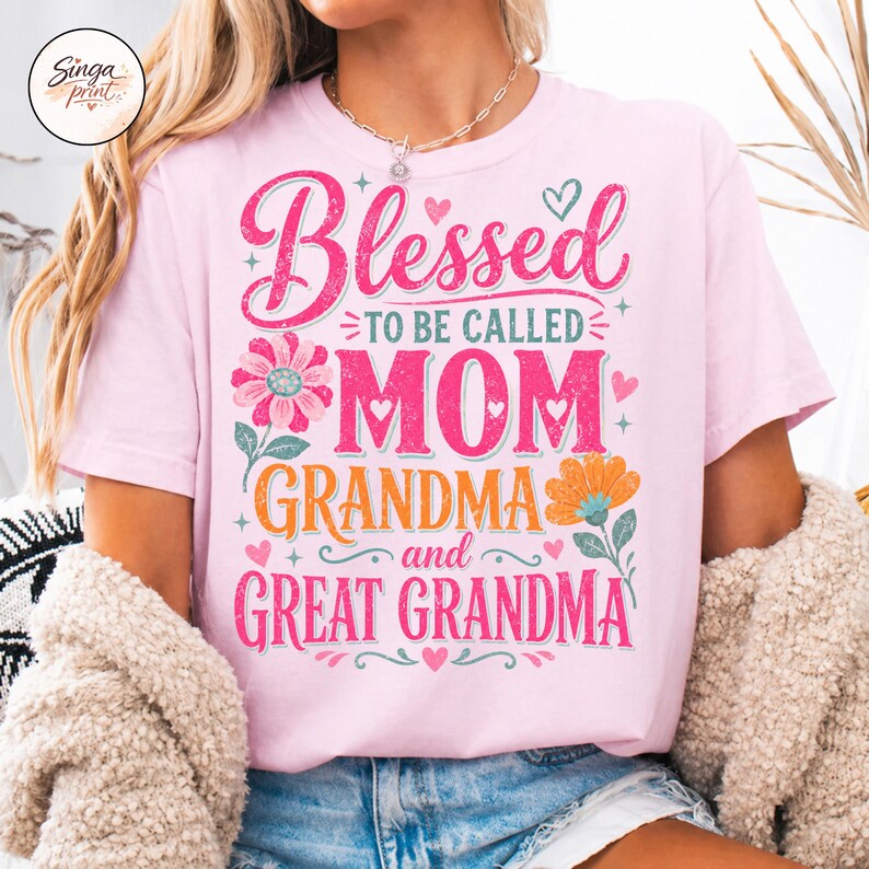 May include: A pale pink t-shirt featuring the text "Blessed to be called Mom Grandma and Great Grandma" in pink script. The design incorporates floral and heart motifs. This is a casual wear garment.