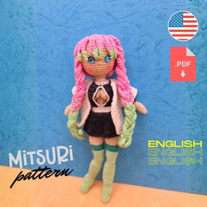 May include: A handmade crochet doll with pink hair, blue eyes, and a black and white outfit. The doll is wearing a white jacket and green socks. The image includes the text "Mitsuri pattern" and "English". A PDF download icon and the American flag are also visible.
