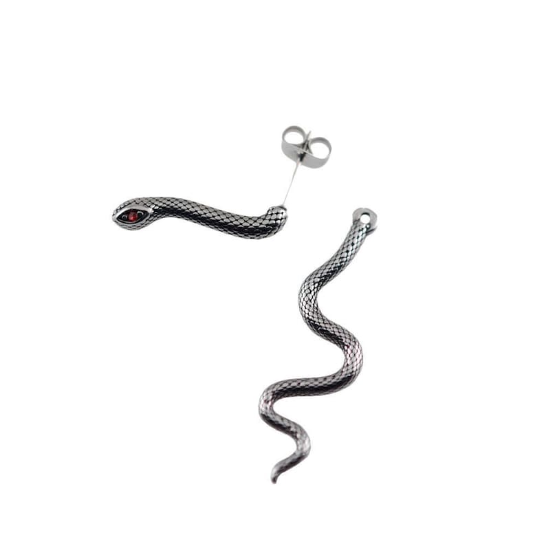 K&ouml;nnte beinhalten: Ein Paar silberfarbene Ohrstecker in Schlangenform mit texturiertem Schuppenmuster und einem kleinen roten Stein im Auge des Schlangenkopfes. Die Ohrringe bestehen aus einem Steckerverschluss und einem langen, gewundenen Schlangenk&ouml;rper aus Metall.