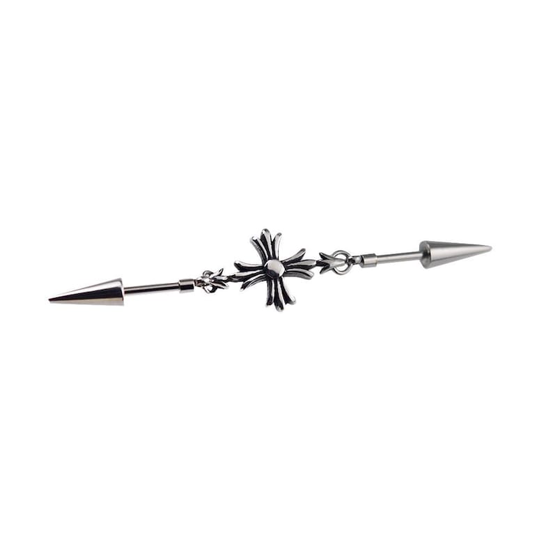 May include: A silver industrial barbell earring with a cross design in the center and a cone-shaped end on each side. The jewelry is made of a shiny metal and is set against a white background.
