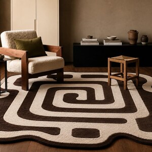 May include: A large, irregularly shaped area rug featuring a bold, dark brown and cream-colored spiral pattern. The rug has a thick, tufted texture with rounded edges and a continuous, winding design that creates a maze-like visual effect on the floor.