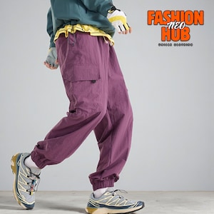 Op de afbeelding: Pruimkleurige cargobroek met een relaxte pasvorm, met een zijzak en elastische manchetten. De broek wordt gecombineerd met grijs-gele sportschoenen. De afbeelding bevat de tekst "FASHION NEO HUB UNIQUE CLOTHING".
