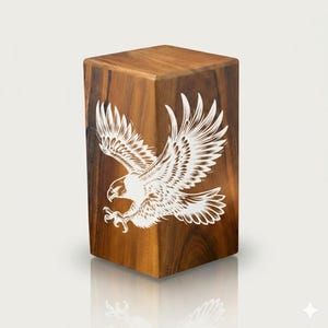 May include: A wooden cube with a detailed white engraving of an eagle in flight. The cube is made of a dark, rich wood with visible grain patterns. The eagle's wings are spread wide, showcasing intricate feather details.