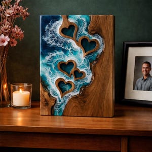 May include: A wooden art piece with a resin design. The piece features a wood grain border with a blue and white resin center, incorporating heart-shaped cutouts. A candle and flowers are in the background.