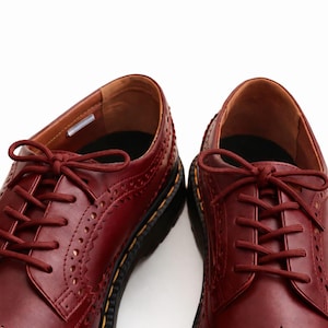 May include: A pair of burgundy leather Oxford shoes with decorative perforations and matching laces. The shoes have a classic design with a rounded toe and a thick black sole with yellow stitching. The interior is a lighter shade of brown.