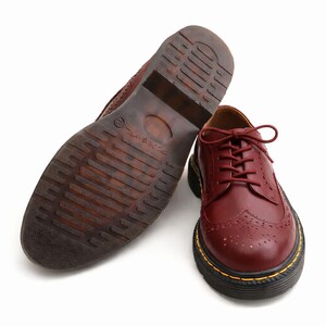 May include: Burgundy leather oxford shoes with a brogue design and a thick black sole with yellow stitching. One shoe is upright, the other is upside down, showing the tread.