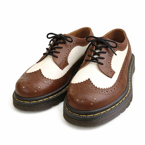 May include: A pair of two-tone brown and white leather brogue shoes with black laces. The shoes have a thick, black sole with yellow stitching and decorative perforations.