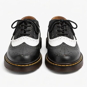 May include: A pair of black and white leather Oxford shoes with decorative perforations and a lace-up closure. The shoes have a thick, brown sole with a yellow accent line. The white sections feature a scalloped edge.