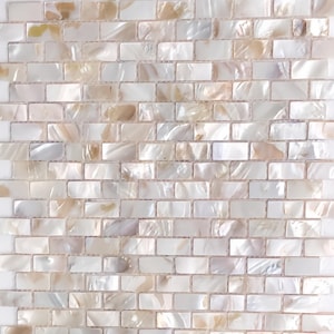 以下が含まれることがあります： 長方形のモザイクタイルのパターンのクローズアップ。タイルは小さく長方形で、レンガのようなパターンに配置されています。タイルは、白、クリーム、タンの色合いで真珠光沢のある虹色の仕上げが施されており、きらめく効果を生み出しています。全体的な効果はエレガントです。