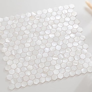 Puede incluir: Mosaico de baldosas hexagonales blancas dispuestas en un patrón de rejilla. Las baldosas tienen un brillo nacarado que refleja la luz. El diseño general es brillante y limpio, adecuado para diversas aplicaciones de diseño de interiores.