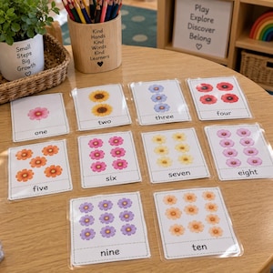 May include: A set of ten rectangular educational flashcards featuring floral illustrations and corresponding number words from one to ten. Each card displays a specific quantity of colorful flowers, including pink, yellow, blue, red, orange, and purple blossoms, arranged in a grid on a white background.