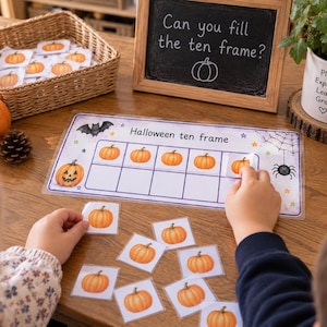 Könnte beinhalten: Ein Halloween Zehnerfeld Lernset bestehend aus einer laminierten rechteckigen Vorlage mit Raster, einer Kreidetafel mit der Aufschrift Can you fill the ten frame?, einem Weidenkorb mit Kürbiskarten und einzelnen Kürbis-Spielkarten.