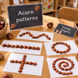 Op de afbeelding: Een verzameling witte kaarten met bruine eikels gerangschikt in verschillende patronen, waaronder een golvende lijn, een rechte lijn, een cirkel, een kruis en een spiraal. Een bordje toont Acorn patterns en een ander Funky fingers.