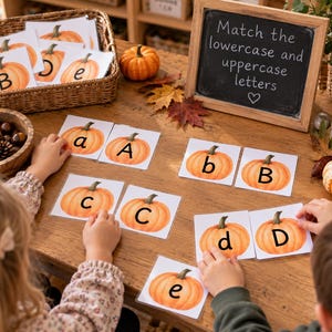 May include: A set of educational flashcards featuring orange pumpkin illustrations with lowercase and uppercase letters. A chalkboard displays the text Match the lowercase and uppercase letters. The cards are arranged on a wooden table.