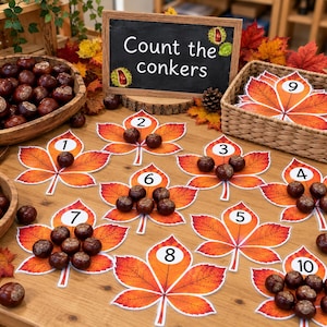 May include: An educational counting activity featuring ten paper autumn leaves, each labelled with a number from one to ten. Brown conkers are placed on the leaves to match the corresponding numbers. A chalkboard sign reads Count the conkers.