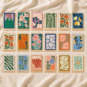 Peut inclure: Une collection de seize cartes d'art floral avec divers motifs. Chaque carte présente une illustration botanique colorée différente, comprenant des fleurs, des feuilles et des fruits, sur des fonds bleus, verts, roses et oranges. Les cartes sont rectangulaires avec une bordure en papier naturel.