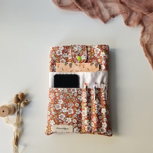 May include: A floral print organizer in shades of brown, white, and yellow, with a green button closure. The organizer holds a smartphone, pens, and a ruler. The text "AtelierHippie" is visible on the bottom.