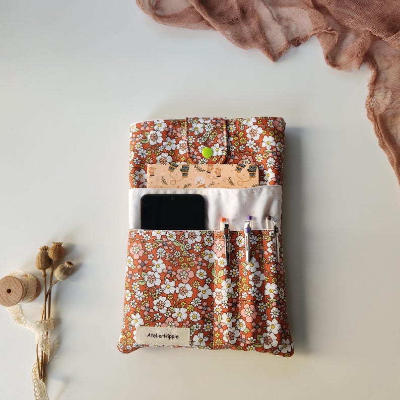 May include: A floral print organizer in shades of brown, white, and yellow, with a green button closure. The organizer holds a smartphone, pens, and a ruler. The text "AtelierHippie" is visible on the bottom.
