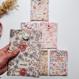May include: A collection of five rectangular fabric pouches featuring various floral patterns in shades of pink, blue, and yellow. Each pouch has a snap button closure and a small rectangular label with the text AtelierHippie.