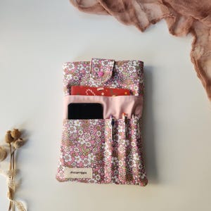 May include: A pink floral fabric organizer with multiple pockets, holding a smartphone, pens, and a small red card. The organizer has a button closure and the text "AtelierHippie" on the front.