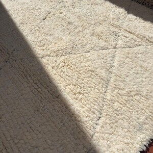 May include: A cream-coloured, textured rug with a diamond pattern. The rug has a thick, plush pile and a fringe along one edge. The rug is made of a soft material, suitable for a living room or bedroom.