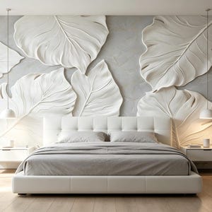 May include: A bedroom featuring a white upholstered bed with gray bedding, flanked by two white nightstands with hanging pendant lights. The wall behind the bed displays a large-scale, three-dimensional white relief sculpture of tropical leaves.