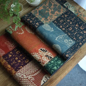 Pode incluir: Uma pilha de quadrados de tecido decorativos com um design de patchwork. Os quadrados apresentam vários padrões, incluindo motivos florais e geométricos, em tons de vermelho, laranja, verde, azul e marinho. Os tecidos parecem ser feitos de um material macio e texturizado.