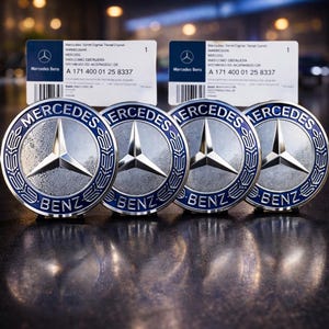 May include: Four silver Mercedes Benz emblems with a blue border and the Mercedes star logo. The word "Mercedes" is at the top and "Benz" at the bottom. Two white cards with text and barcodes are in the background.