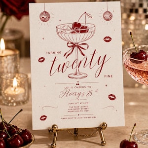 May include: A party invitation card with a cocktail illustration, cherries, and the text "Turning twenty fine". The invitation is on a small gold stand, with cherries and a glass of cocktail in the background.
