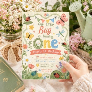 May include: A rectangular birthday invitation card featuring colorful illustrations of ladybugs, butterflies, a dragonfly, and various flowers. The text reads: Our Little Bug is Turning One, Piper's 1st Birthday, Saturday, August 9, 1:00 PM - 4:00 PM, 18 Daisy Hollow Lane, Charleston, SC 29403, RSVP to Natalie at 555-0136.