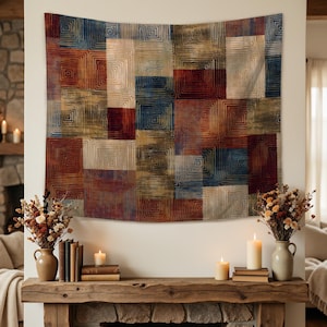 May include: A large, rectangular tapestry with a geometric pattern of squares in shades of red, blue, gold, and beige hangs on a white wall. The tapestry is the focal point, with a rustic wooden mantel below, adorned with candles and vases.