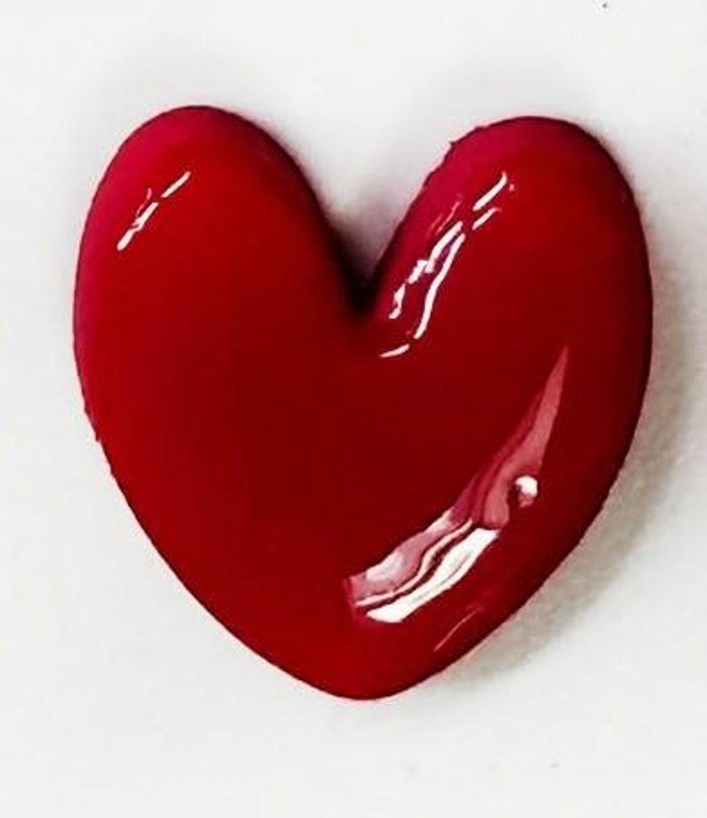 May include: A three-dimensional heart-shaped object with a smooth, glossy, deep red finish. The surface reflects light, creating bright white highlights that emphasize the rounded, puffed contours of the heart shape.