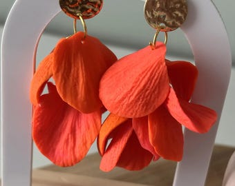 Puede incluir: Un par de pendientes colgantes con componentes en forma de pétalo de color naranja brillante suspendidos de tachuelas circulares de metal dorado con un acabado martillado. Los pétalos naranjas están superpuestos para crear volumen.