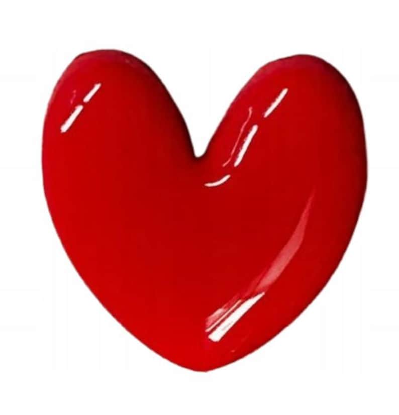 May include: A solid, bright red heart-shaped object with a smooth, glossy, and reflective surface. The heart features a rounded top with two distinct lobes and a pointed bottom, creating a classic, symmetrical heart silhouette.