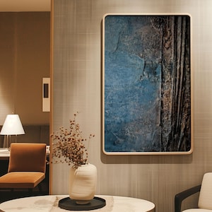 Könnte beinhalten: Abstrakte Wandkunst mit einem strukturierten Design in Blau-, Braun- und Schwarztönen, gerahmt in hellem Holz. Das Kunstwerk hängt an einer strukturierten grauen Wand, mit einer Vase mit getrockneten Blumen und einer Lampe im Raum.