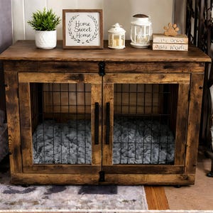 May include: A rustic wooden dog crate with a distressed finish. The crate features two doors with wire mesh panels and a plush gray bed inside. A framed sign that says "Home Sweet Home" sits on top, along with decorative lanterns and a potted plant.