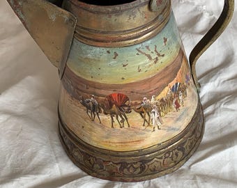 May include: A vintage metal pitcher with a weathered brass finish, featuring a hand-painted desert scene with camels and figures in traditional attire. The vessel has a wide spout, a curved handle, and an ornate, embossed band around the base.
