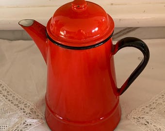 May include: A bright orange enamel coffee pot with a matching lid and a black handle. The pot features a tapered cylindrical body, a curved spout, and a black rim detail around the lid and the base of the handle, showcasing a glossy finish.