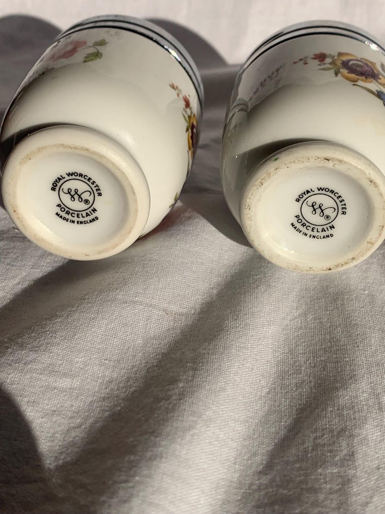 May include: Two white porcelain egg coddlers featuring colorful floral patterns and silver-tone metal lids. The base of each piece is stamped with the Royal Worcester logo, the text Porcelain, and Made in England, indicating their origin.