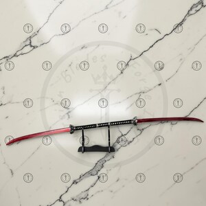May include: A double-edged sword with a red blade and black handle, displayed on a black stand. The blade has a curved design, and the handle is detailed with silver accents. The sword is set against a white marble background.