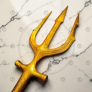 May include: A golden trident with three prongs and a textured handle. The trident is a bright, shiny gold color and is set against a white and gray marble background. The trident is a symbol of power and authority.