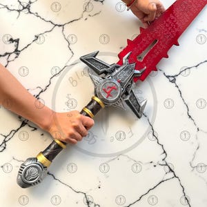 May include: A large, ornate sword with a red blade and intricate silver and gold detailing. The hilt features a circular emblem with a red symbol. The blade has etched inscriptions.