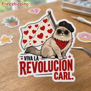 May include: A die-cut sticker featuring a fluffy tan cat wearing a black beret with a red star, round sunglasses, and a red neckerchief. The cat holds a white flag patterned with red hearts. Below, the text reads VIVA LA REVOLUCION CARL.