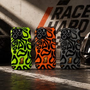 Peut inclure: Trois coques de smartphone avec un motif abstrait ondulé noir sur des fonds vert néon, orange vif et gris foncé. Chaque coque présente un chiffre un doré en bas et une petite icône de visage souriant sur le côté droit.
