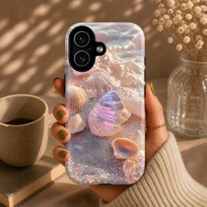 Può includere: Una custodia per telefono con un design a tema spiaggia, che mostra conchiglie e sabbia scintillante. La custodia ha una finitura lucida e un'apertura per la fotocamera. Il design incorpora conchiglie nei toni del bianco, rosa e iridescenti, evocando un'estetica costiera.