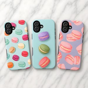 May include: Three phone cases with colorful macaron designs. One case is light blue with scattered macarons. Another is light blue with three macarons. The third case is lavender with pink macarons.